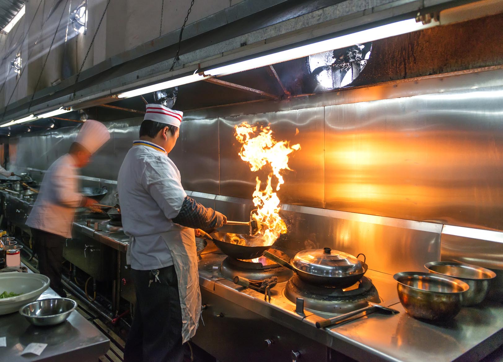 Asian chefs cooking in restaurant kitchen with giant flame coming out of a wok. Gourmet Spice Company, Wholesale Food Distributor.