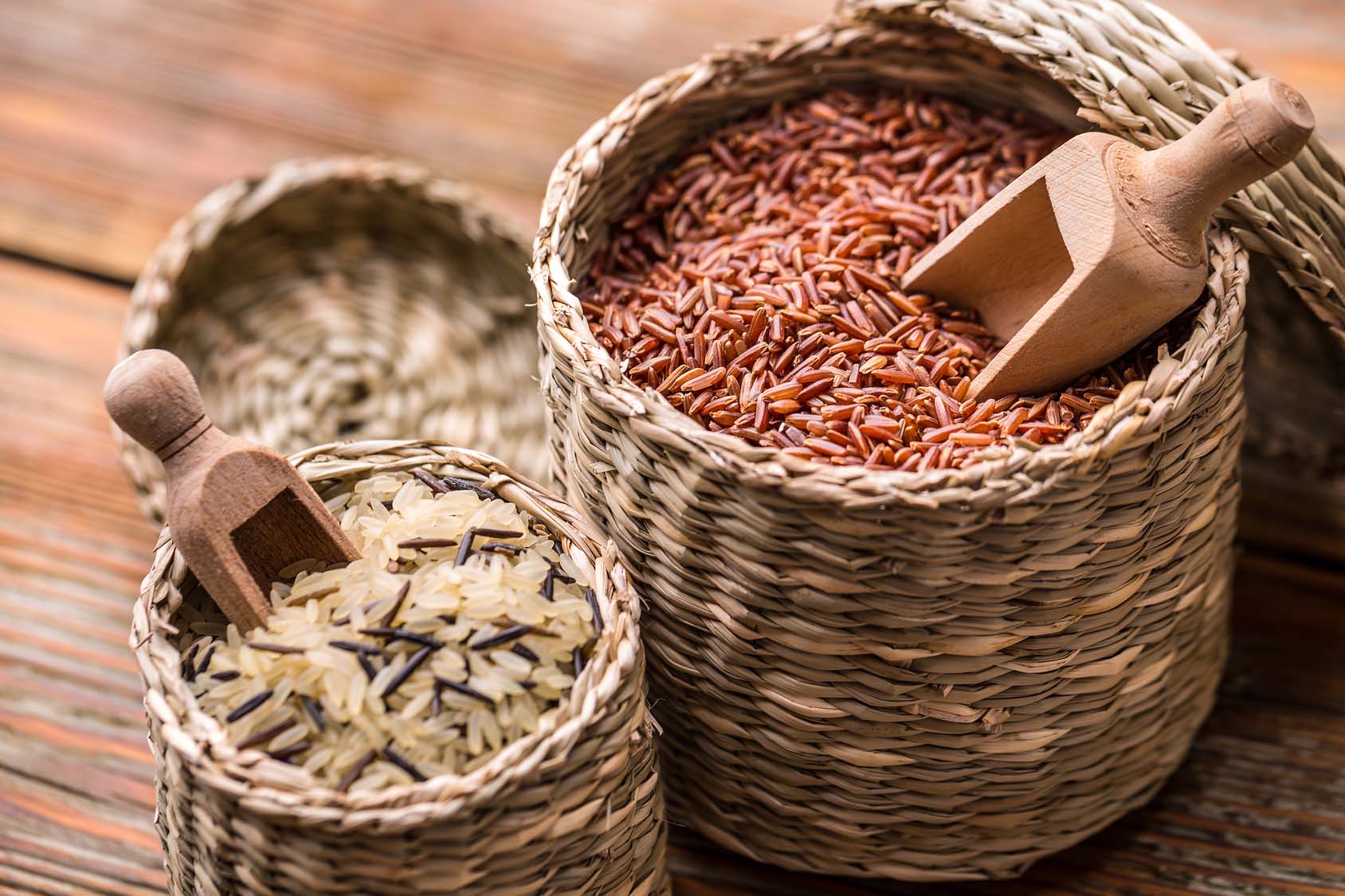 Colorful rice grains in wicker backets with wooden scoops. Gourmet Spice Company, Wholesale Food Distributor.