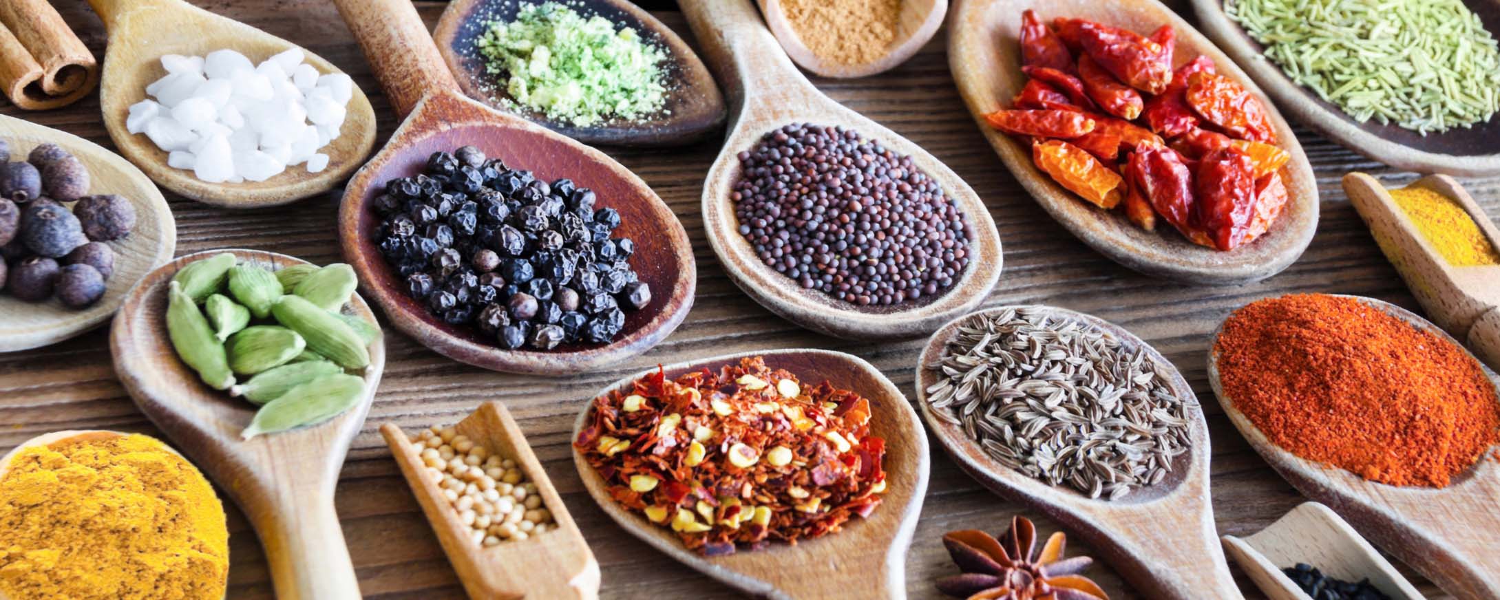 Variety of colorful, dried herbs and spices on wooden spoons. Gourmet Spice Company, Wholesale Food Distributor.