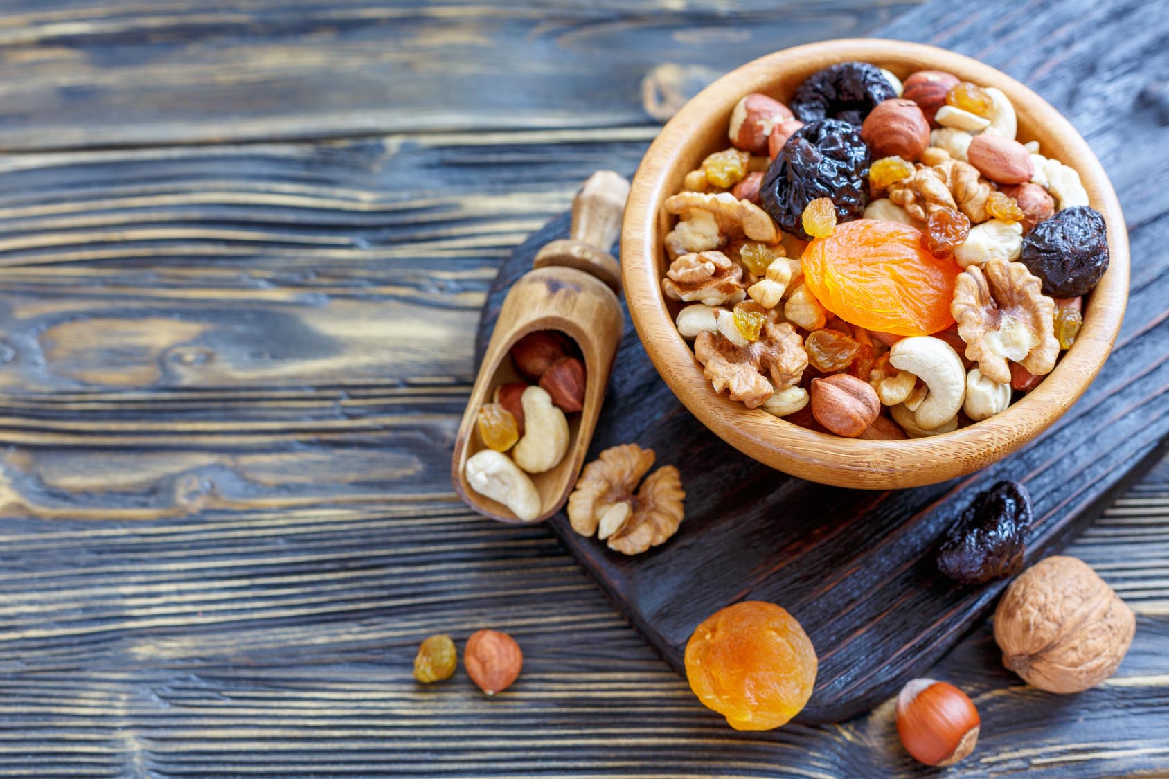 Trail mix in bowl and scattered nuts and dried fruit on wooden grey-washed counter. Gourmet Spice Company, Wholesale Food Distributor.